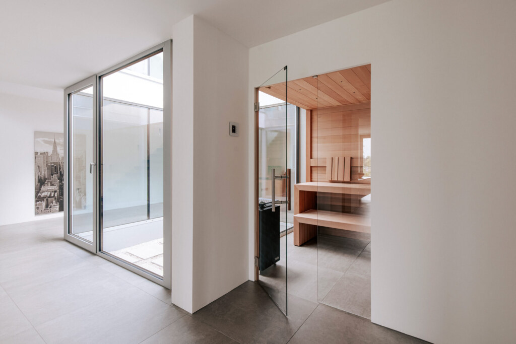 Minimalistische, moderne Sauna aus ruhig anmutendem Zedernholz, mit Glasfront und Anbindung an ein rundum verglastes Atrium.