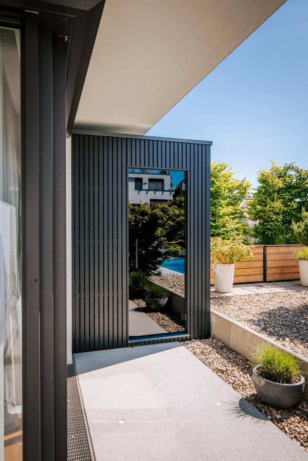 Kleine schwarze Außensauna in puristischem Design und mit verspiegelter Glastüre auf einer Terrasse in einem Steingarten.