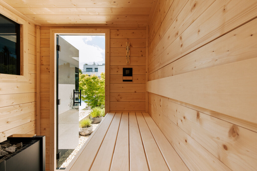 Sauna aus hellem Fichtenholz mit Ausblick in einen Steingarten mit Pool.