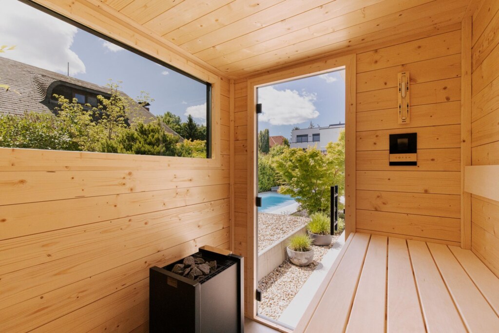 Sauna aus hellem Fichtenholz mit Ausblick in einen Steingarten mit Pool.