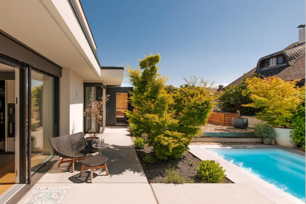 Schwarz verkleidete Outdoorsauna auf einer Terrasse im Steingarten mit Sitzgarnitur und Pool.