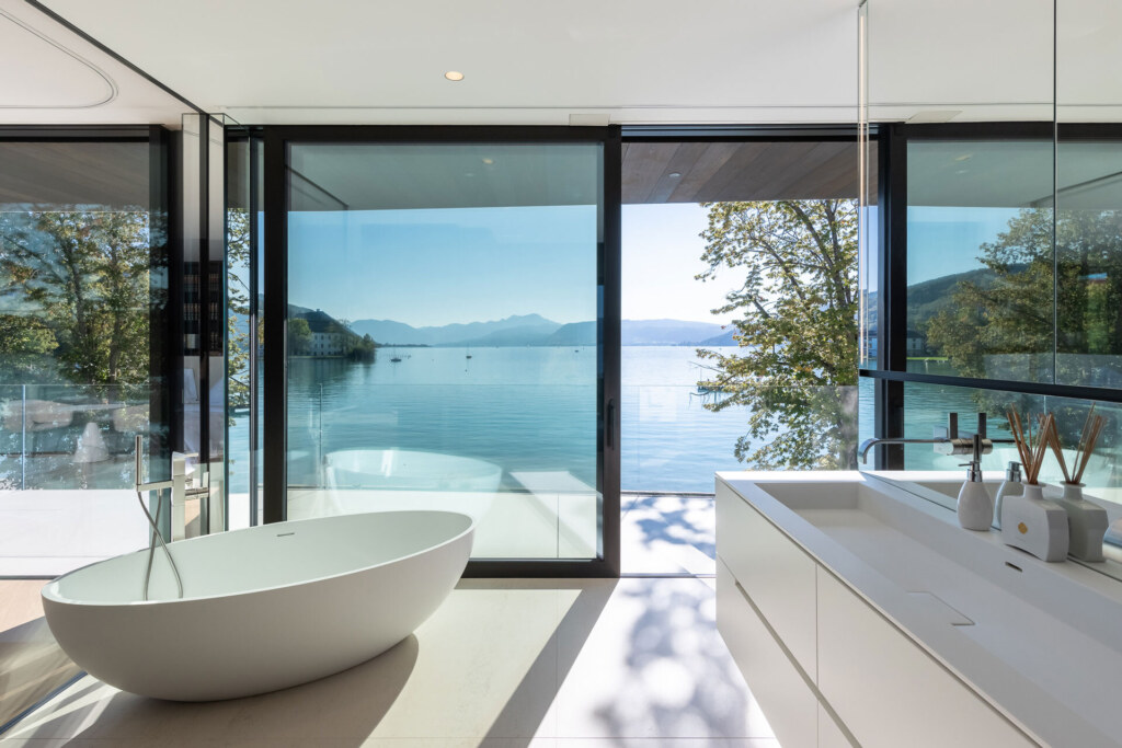 Luxusbadezimmer mit freistehender Badewanne, einem minimalistischen Waschtisch und Ausblick auf einen See.
