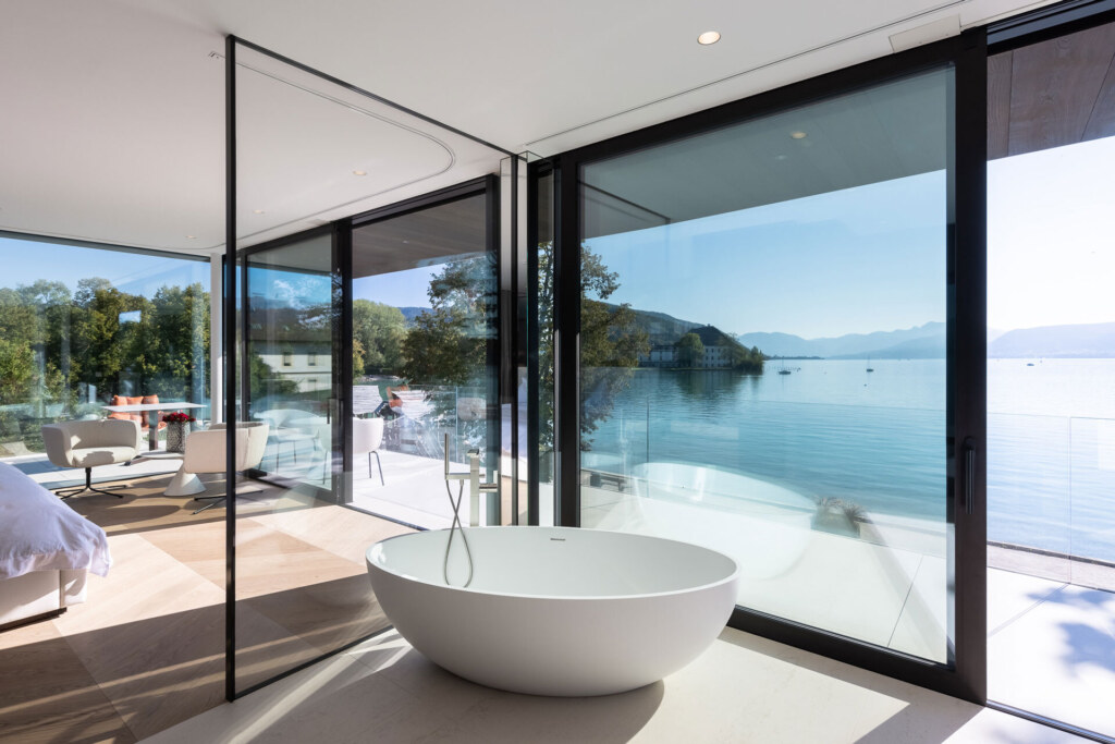 Luxusbadezimmer mit freistehender Badewanne, großflächiger Fensterfront und Seeblick.