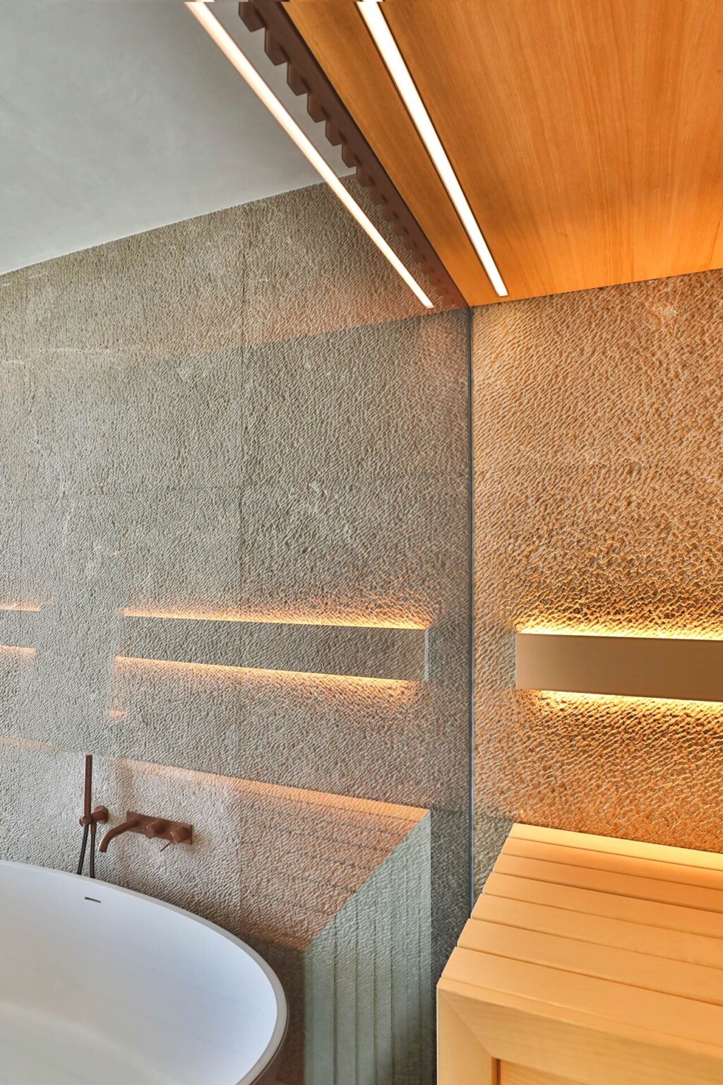 Bleuchtete, moderne Sauna aus hellem Holz mit integrierter Natursteinwand und getönter Verglasung.