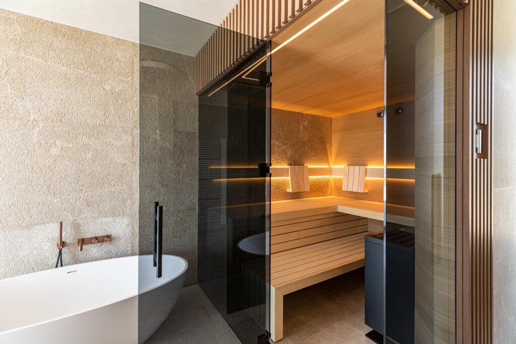 Moderne Sauna mit getönter Frontverglasung und strukturierter Holzverkleidung, innen ausgeführt in gemaserten, astfreien Eichenholzpaneelen und direkter Anbindung an eine strukturierte Natursteinwand.