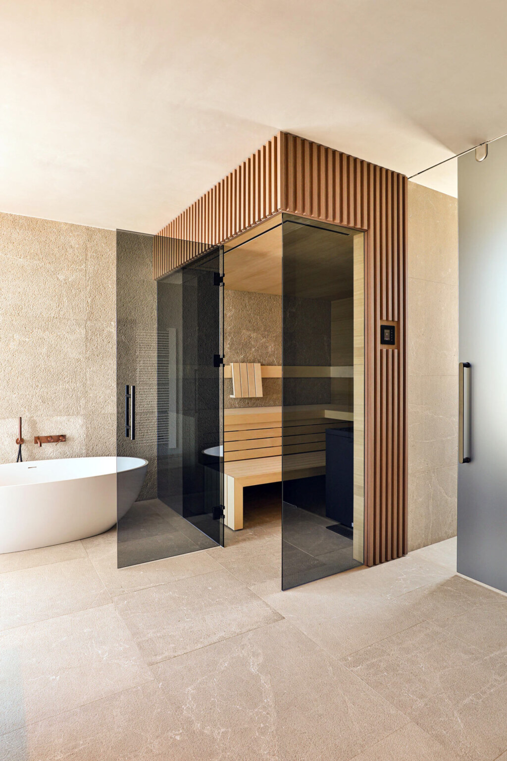 Minimalistische Sauna mit schwarz getönter Frontverglasung, verkleidet in getönten Holzleisten, innen ausgeführt in gemaserten, astfreien Eichenholzpaneelen in einem Badezimmer mit freistehender Badewanne im Japandi Stil.