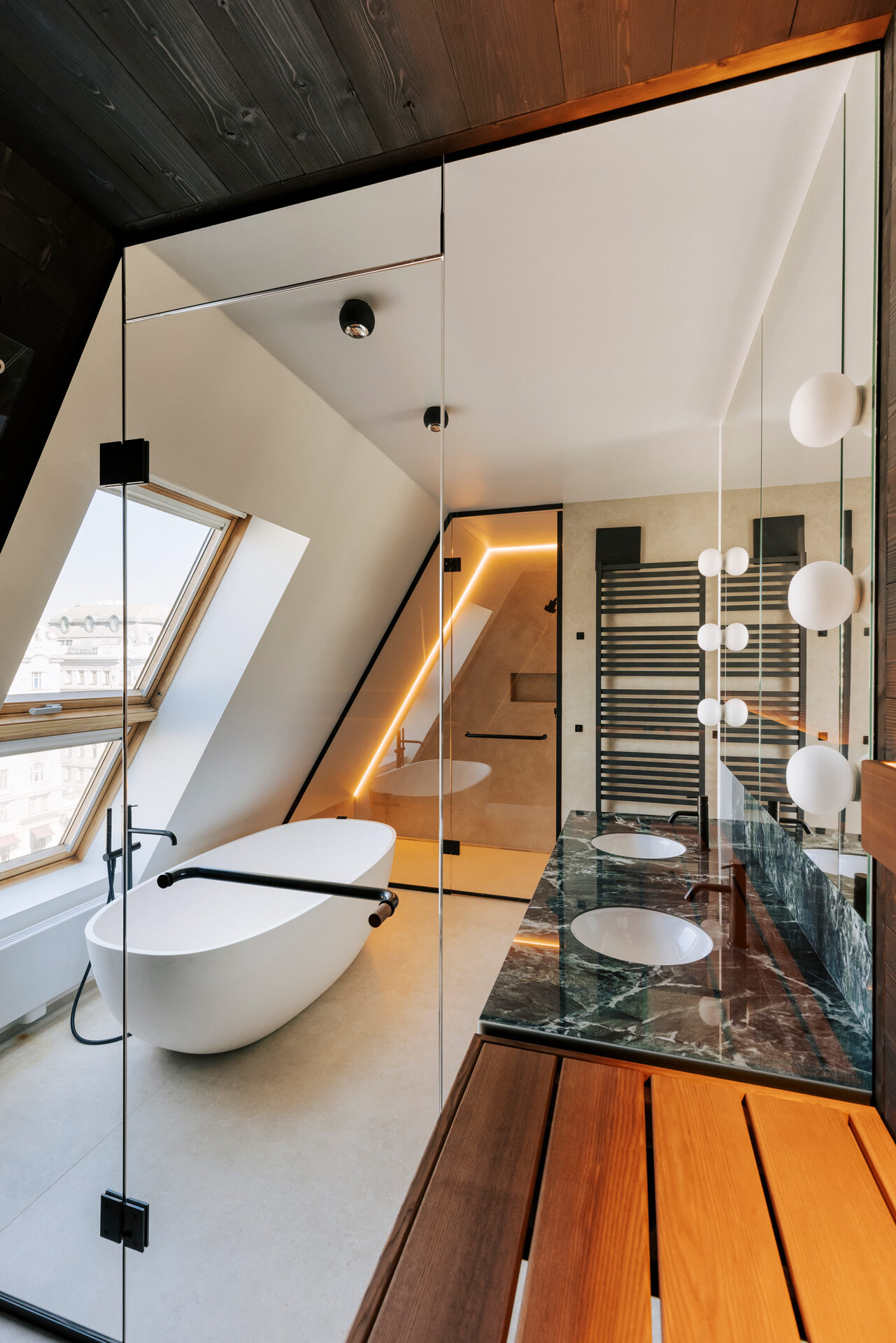 Blick aus einer maßgeschneiderten Sauna in ein luxuriöses Badezimmer einer Dachwohnung mit freistehender Badewanne und dezent beleuchteter Dusche.