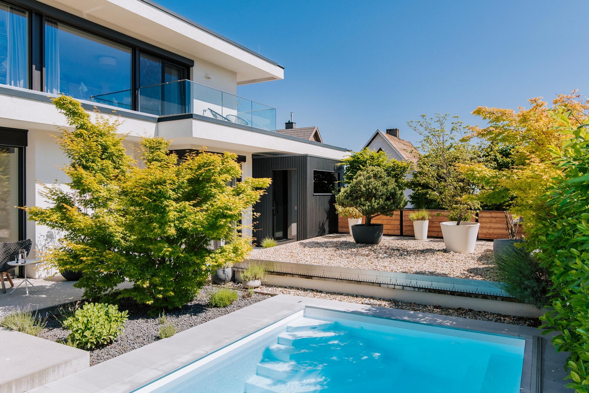 Schwarze Sauna in geradlinigen, minimalistischem Design, harmonisch in die moderne Architektur des Hauses eingebettet. Pool, Balkon und Steingarten ergänzen die private Wellnessoase.