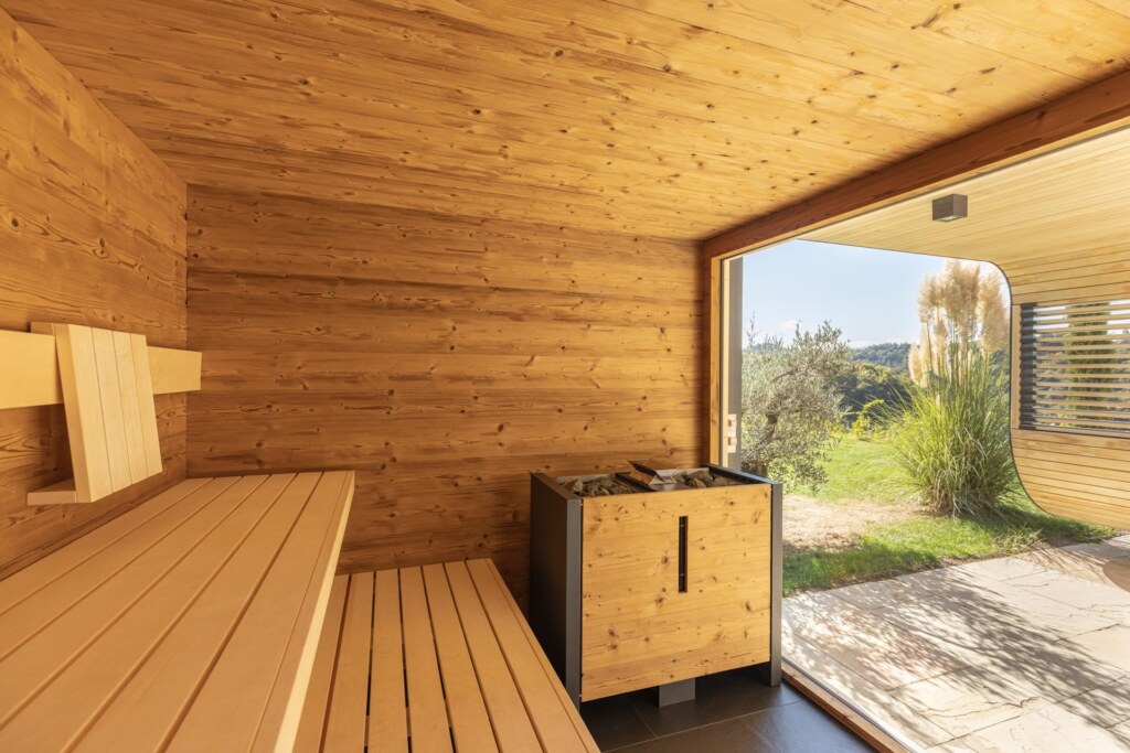 Sauna von Deisl aus Thermo-Fichte mit einem großem Panoramafenster und Blick auf die Terrasse und einen mediterranen Garten.