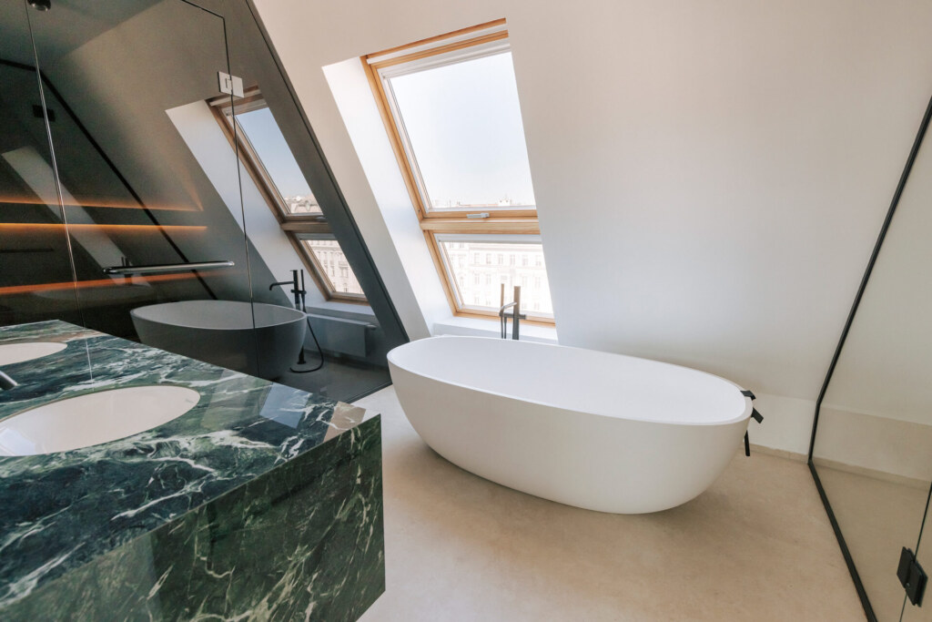 Modernes Badezimmer mit freistehender Badewanne unter einem Dachfenster, einem Waschtisch aus grünem Marmor und einer Sauna mit dunkler Verglasung unter einer Dachschräge.