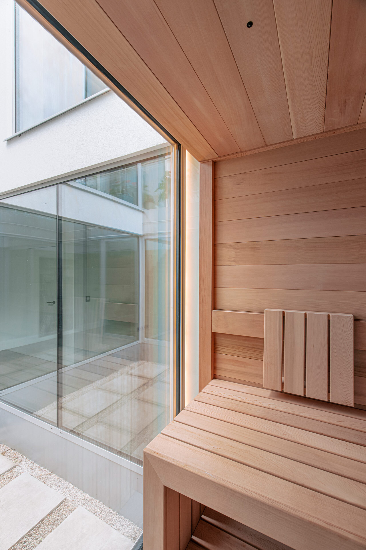 Sauna von Innen aus rötlich anmutendem Zedernholz ohne Maserung, mit Lichtleiste und Anbindung an ein vollverglastes Atrium.