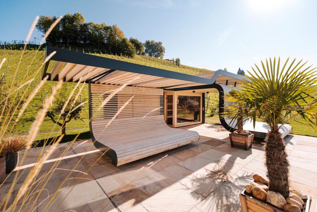 Moderne Außensauna in hellem Holz mit integrierten wellenförmigem Liegeflächen auf einer Terrasse mit mediterranem Flair.