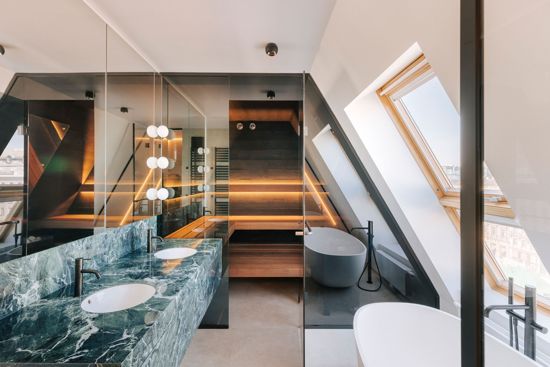 Dunkel verglaste und dezent beleuchtete Sauna mit Marmorwaschtisch und freistehender Badewanne in einem luxuriösen Badezimmer einer Dachgeschosswohnung.