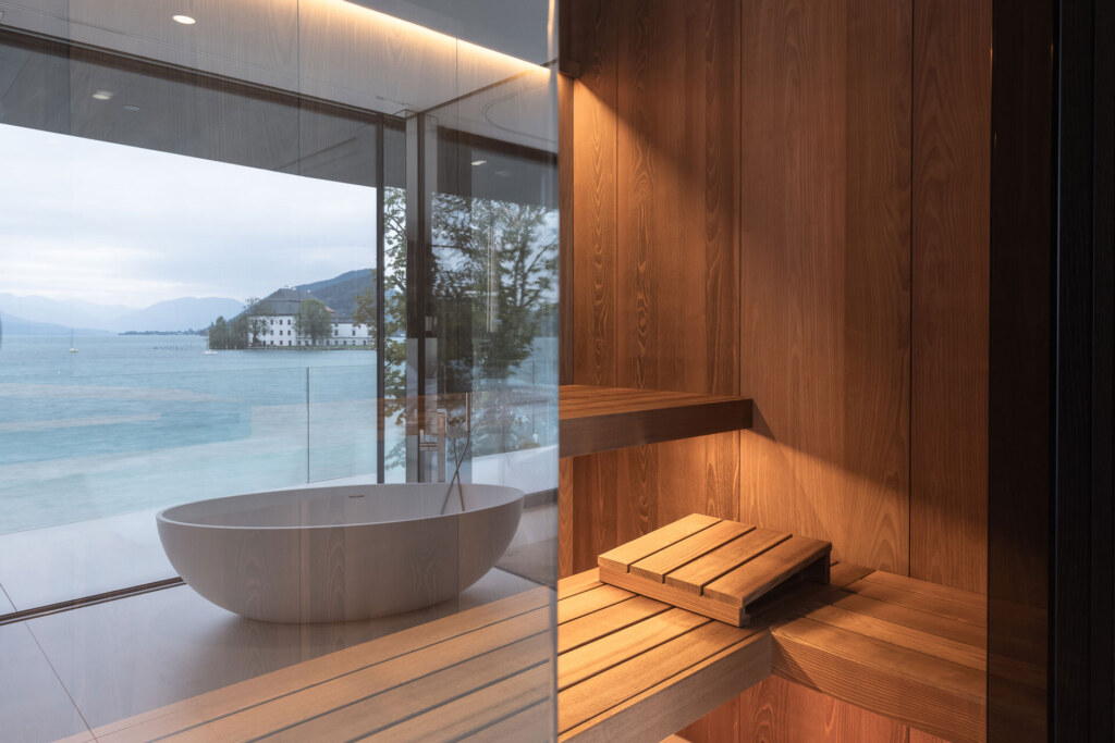 Sauna in minimalistischem Design im Luxusbadezimmer mit freistehender Badewanne und Blick auf den See.