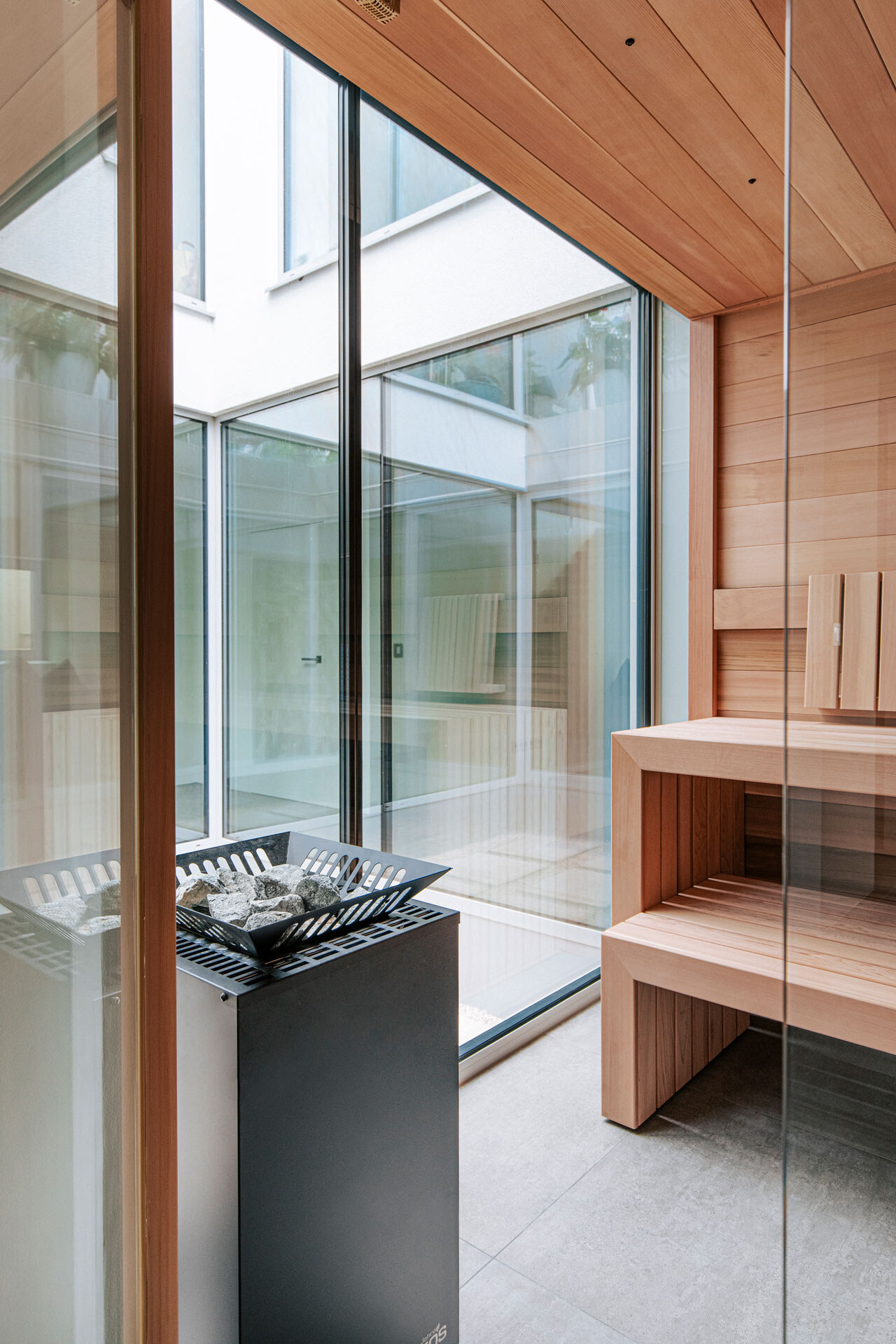 Puristische Design-Sauna aus kanadischem Zedernholz mit einem freistehenden Saunaofen und rahmenloser integriertes großes Panoramafenster .