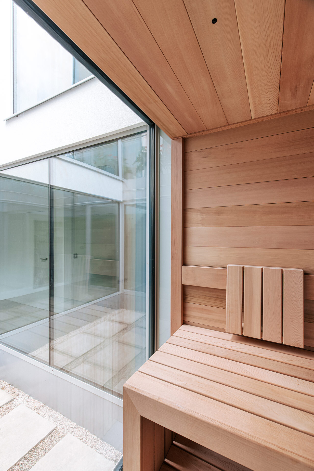 Maßgeschneiderte Sauna aus ruhig gemasertem, astfreiem Zedernholz mit rahmenloser Anbindung an ein Fenster zum Lichthof.