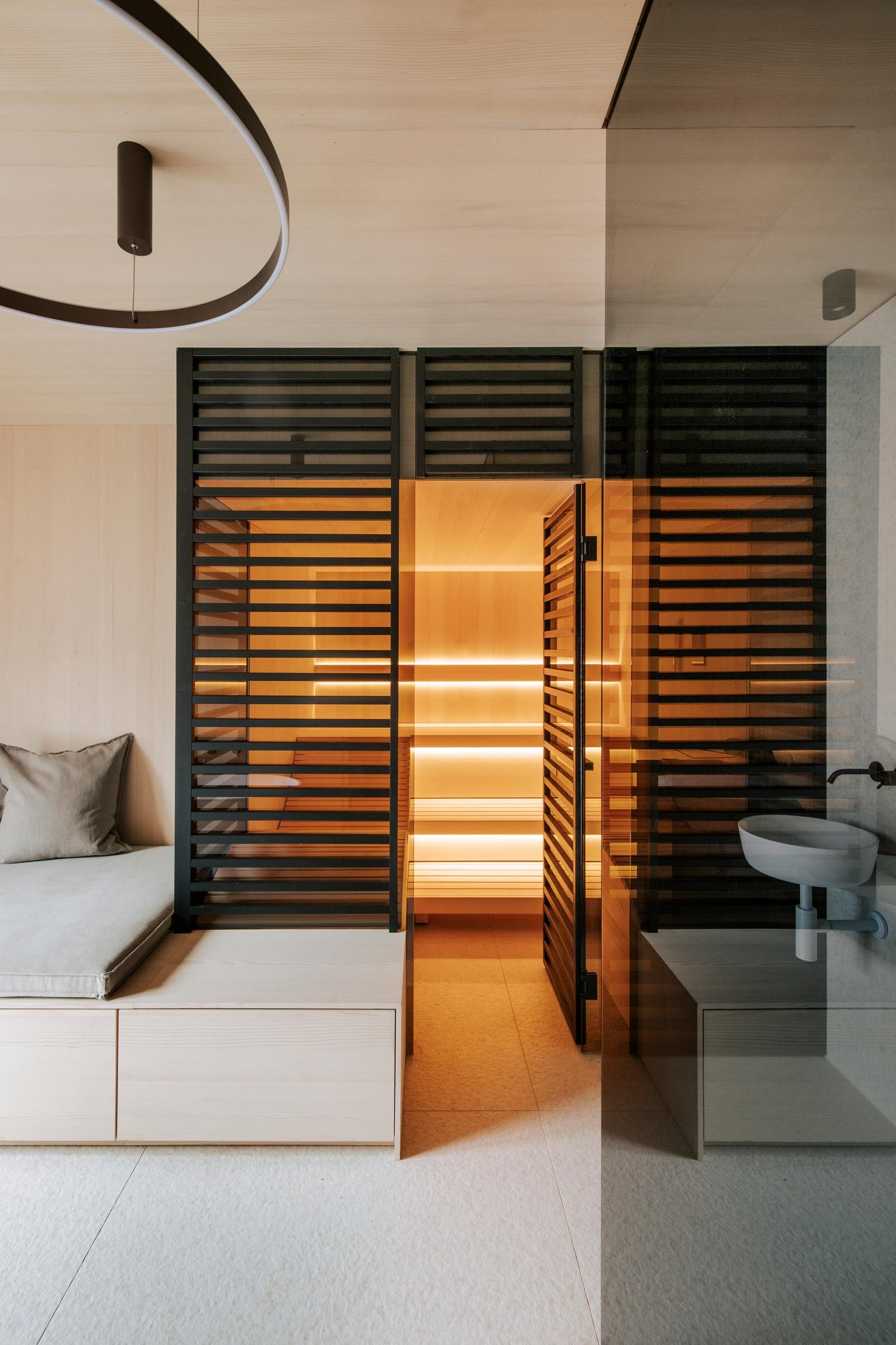 Beleuchtete Sauna im Japandi Stil vom Saunahersteller Deisl, mit raumhoher Verkleidung aus schwarzen Holzstreben als Sichtschutz im Badezimmer mit heller Holzverkleidung.