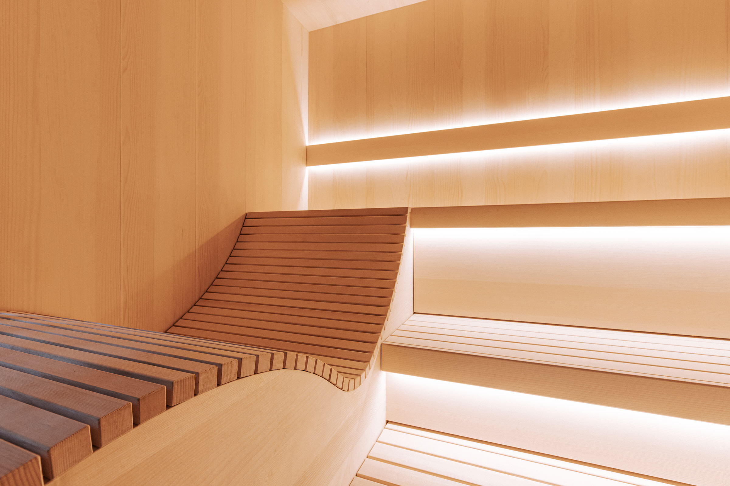 Innenraum einer puristischen Sauna aus gesaegtem Tannenholz mit dezenter Beleuchtung, ergonomischer Saunaliege und Saunabaenken aus Espenholz, der oesterreichischen Sauna Marke Deisl.