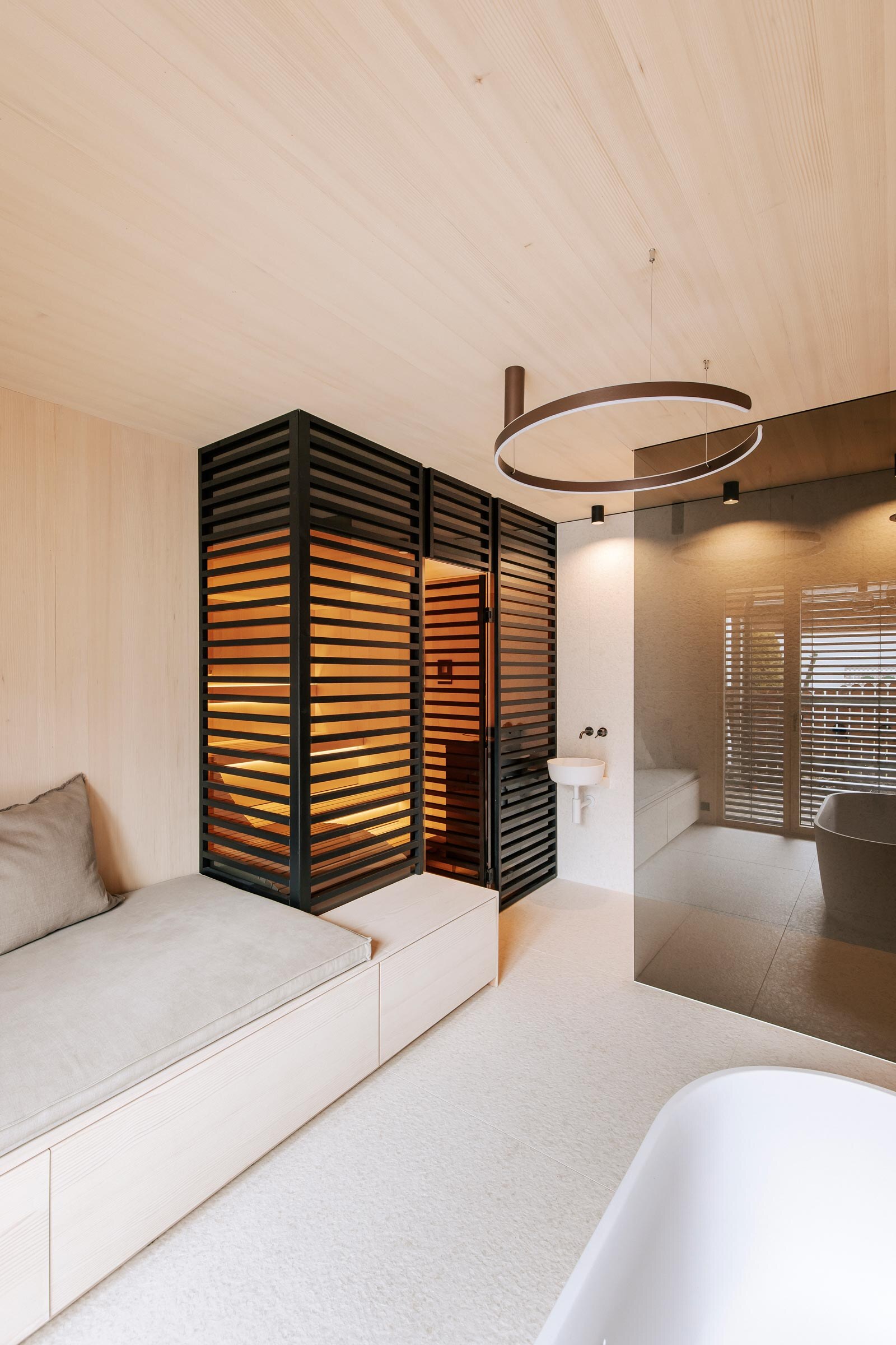 Modernes Private Spa im Badezimmer mit maßgeschneiderter Sauna mit getoenter Panorama-Glasfront, sowie raumhoher Verkleidung aus schwarzen Holzstreben als Sichtschutz, anschliessendem Daybed und bodengleicher Dusche.