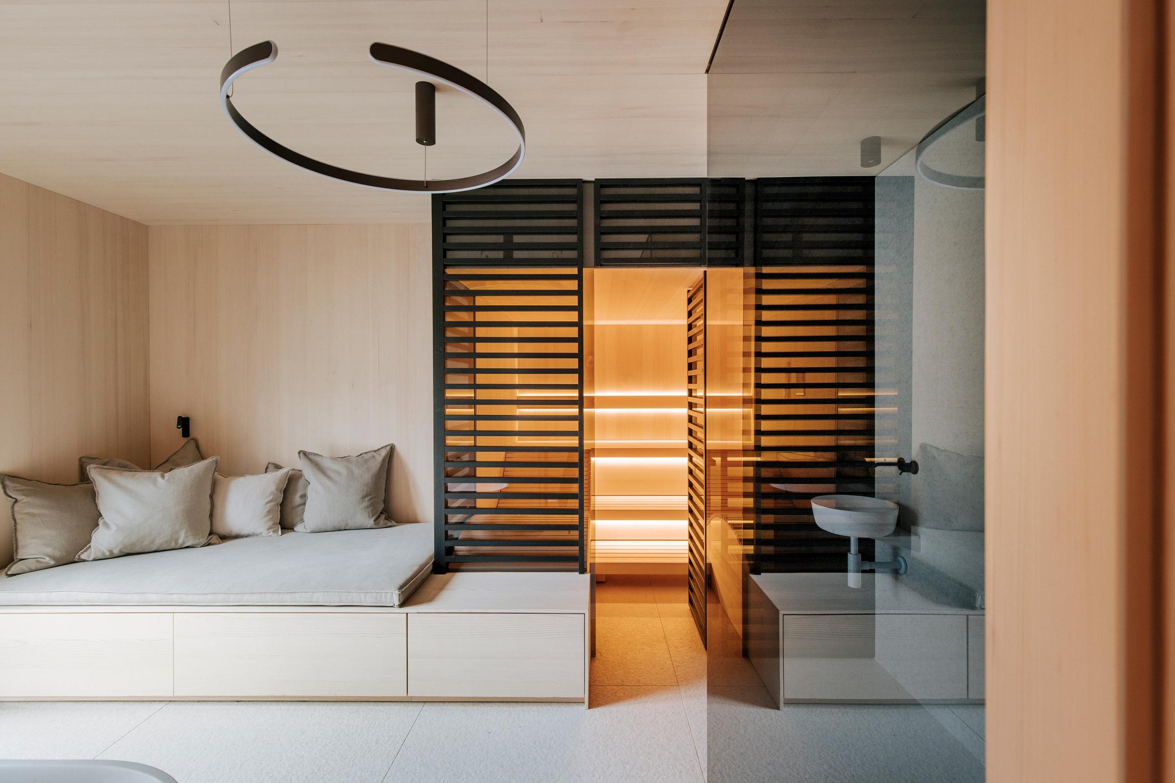 Beleuchtete Sauna von Deisl im minimallistischen Scandi Stil, mit schwarzer Holzverkleidung als Sichtschutz in einem Badezimmer mit heller Holzverkleidung.