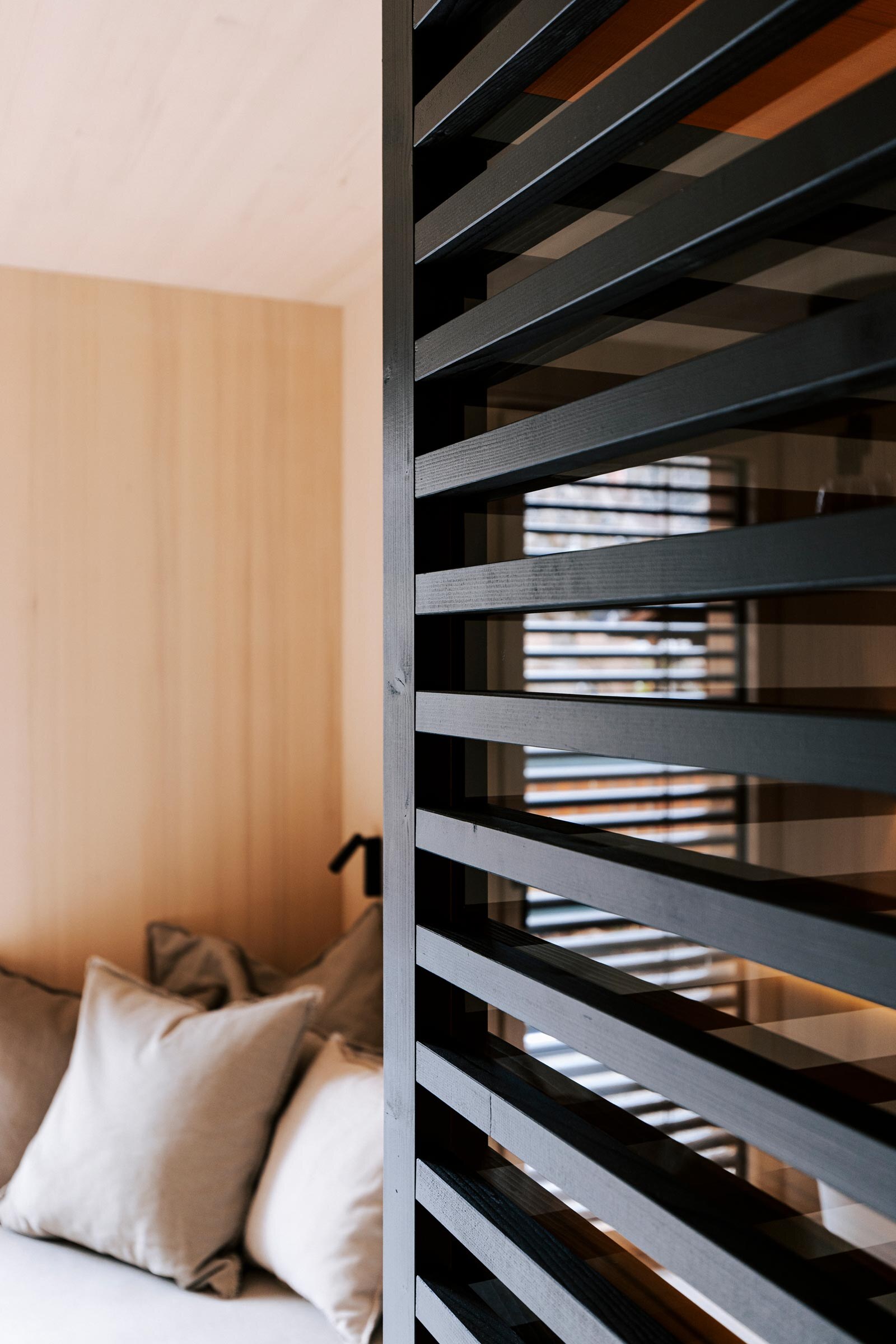 Schwarz getoente Holzstreben-Verkleidung als Sichtschutz einer modernen Sauna mit anschliessendem Daybed.