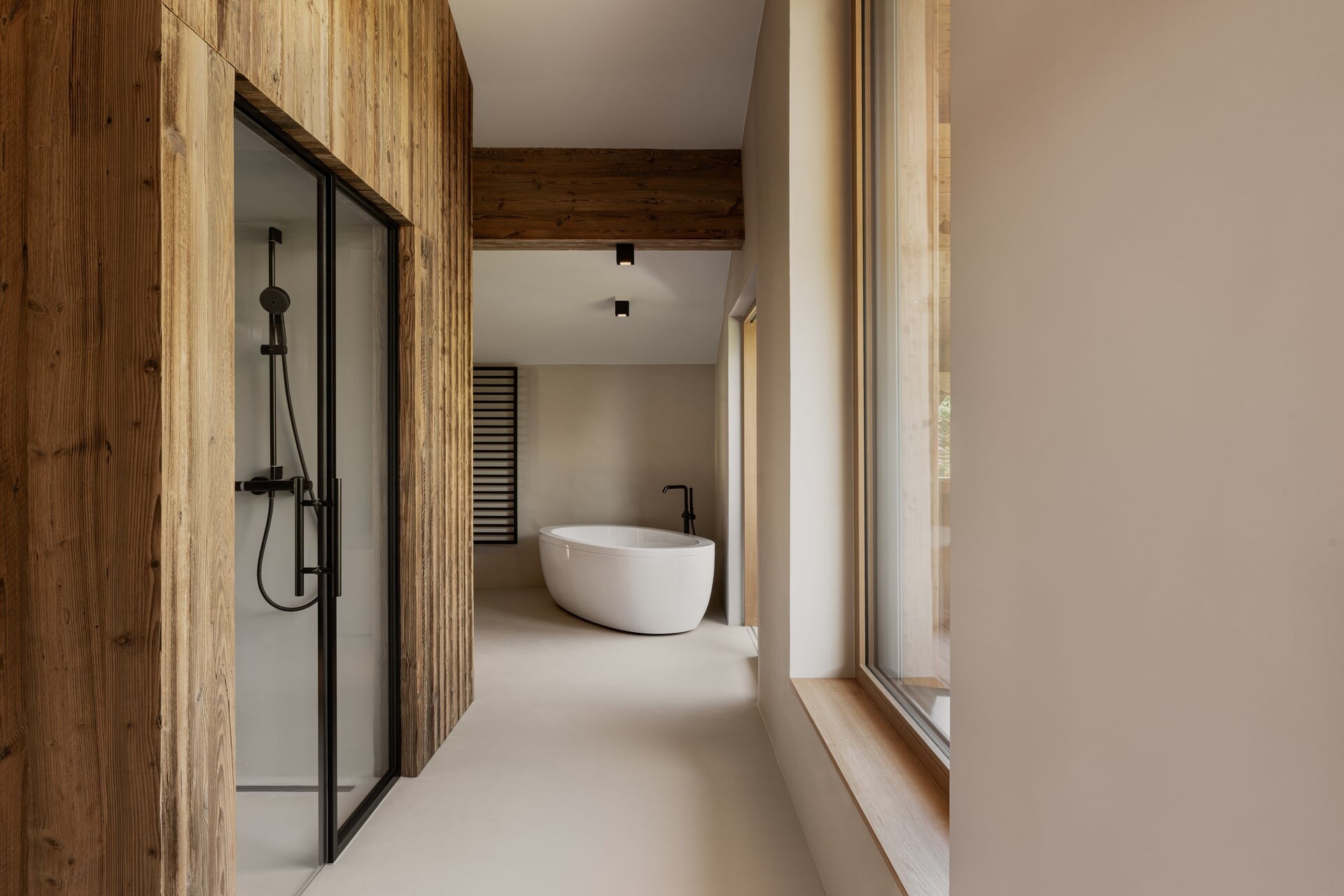 Moderne Dampfdusche aus Mikrozement mit Glasfront und schwarzen Armaturen im minimalistisch-alpinem Badezimmer mit freistehender Badewanne.