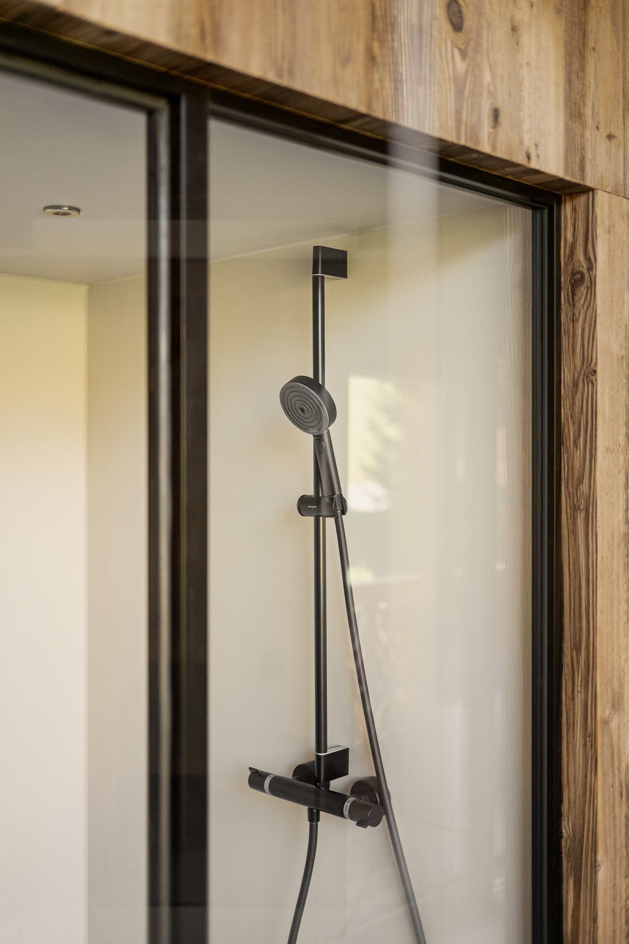 Moderne Dampfdusche aus Mikrozement mit Glasfront, schwarzen Armaturen und Holzverkleidung im Badezimmer in minimalistisch-alpinem Stil.