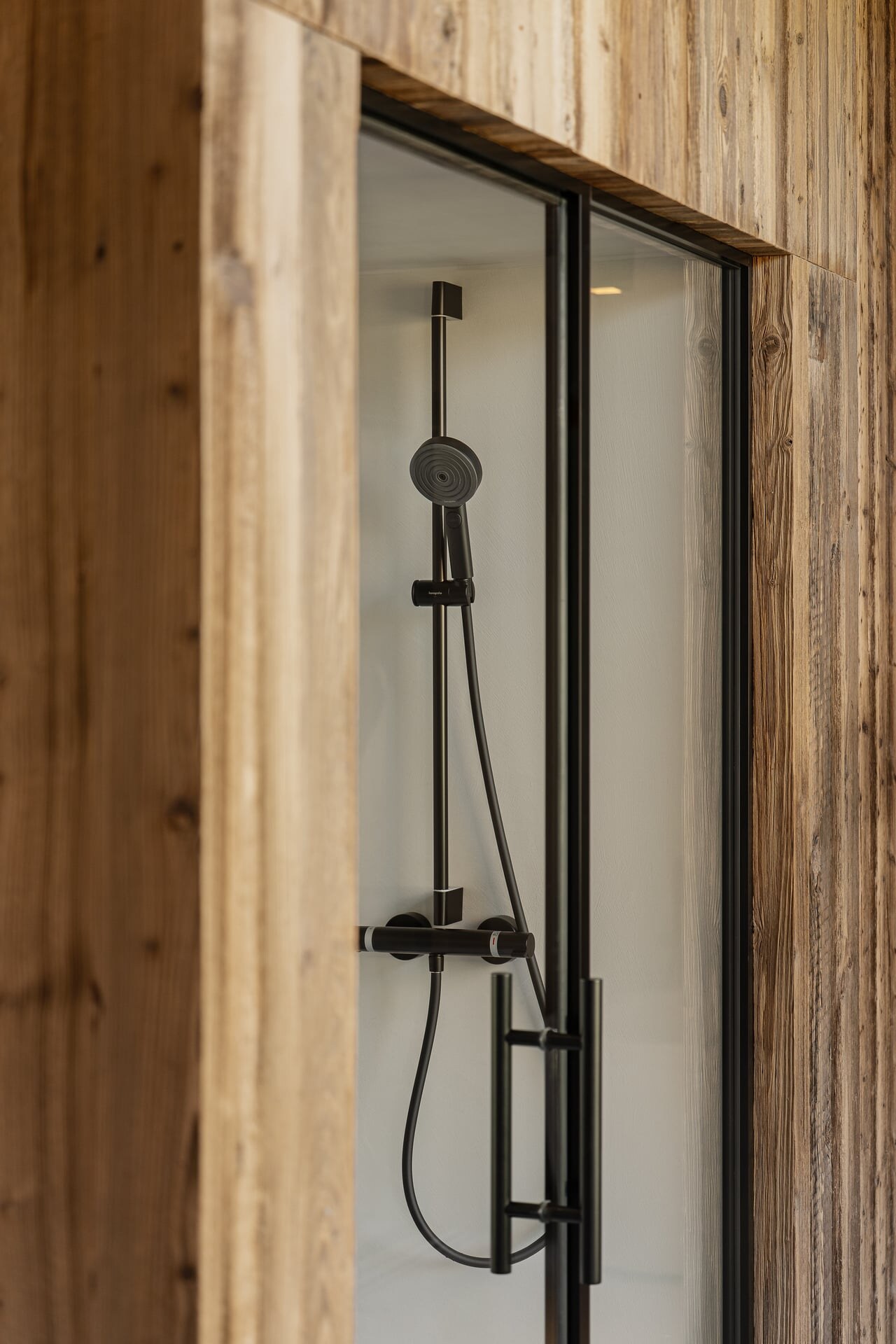Luxus-Dampfdusche aus Mikrozement mit Glasfront, schwarzen Armaturen und Holzverkleidung im Badezimmer in minimalistisch-alpinem Stil.