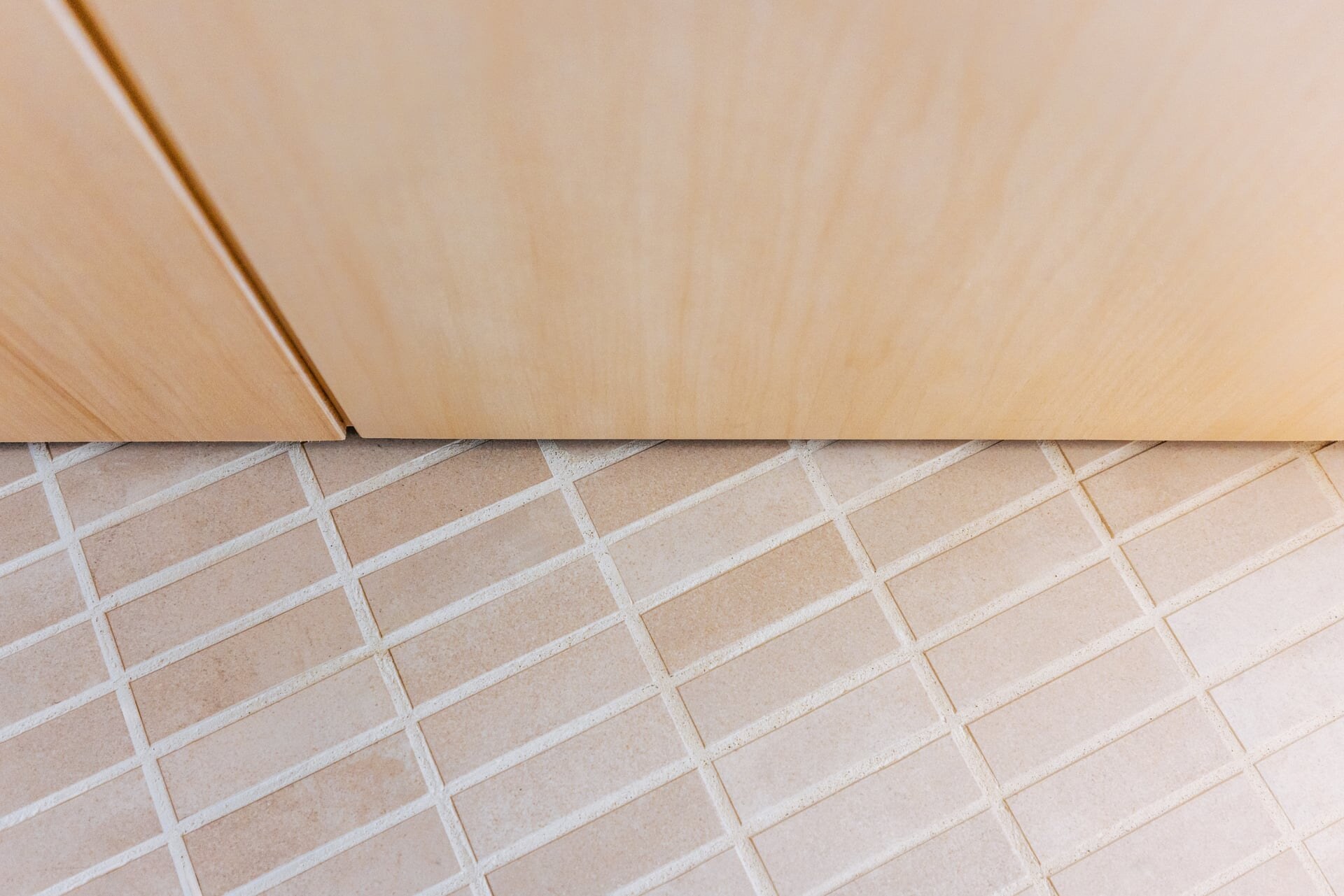 Materialdetail einer Sauna aus hellem Espenholz mit Boden aus hellrosa Mosaikfliesen.