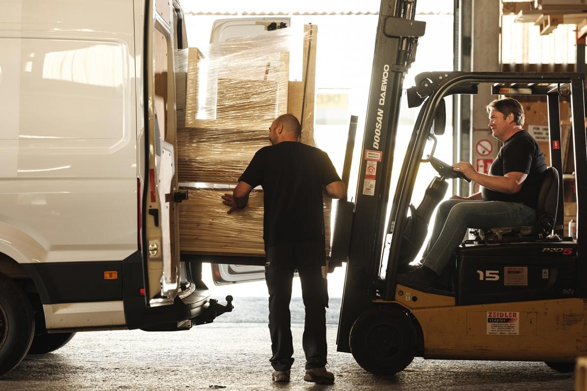 Zwei Deisl Monteure beim Beladen eines weißen Montagebus mit Saunabauteilen mit einem Gabelstapler.