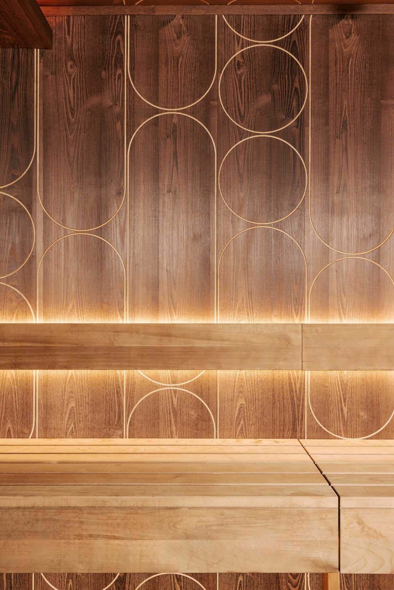 Saunabank einer Design-Sauna aus dunklem Akazienholz mit dekorativen Fräsungen an der Wand.