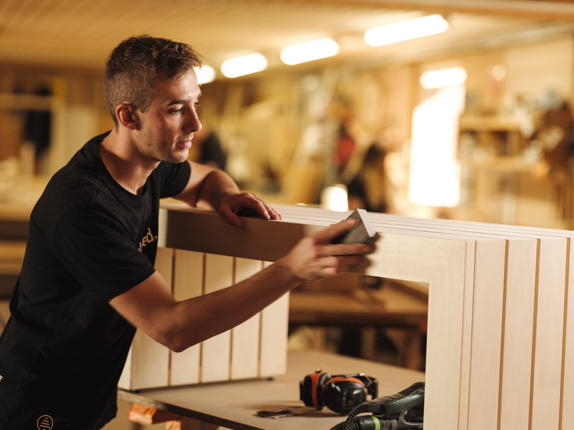 Ein Deisl Tischler schleift eine Saunabank aus hellem Holz in der Saunaproduktion.