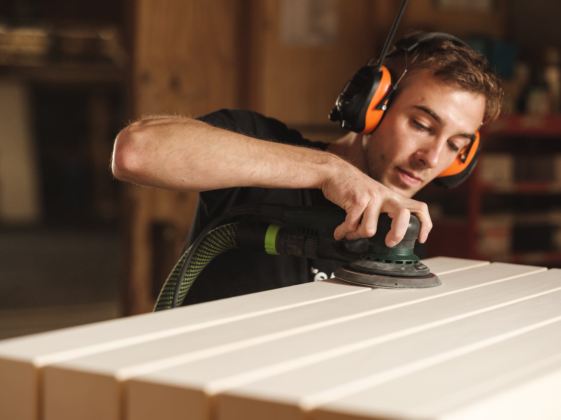 Ein Deisl Tischler schleift eine Saunabank aus hellem Holz in der Saunamanufaktur.