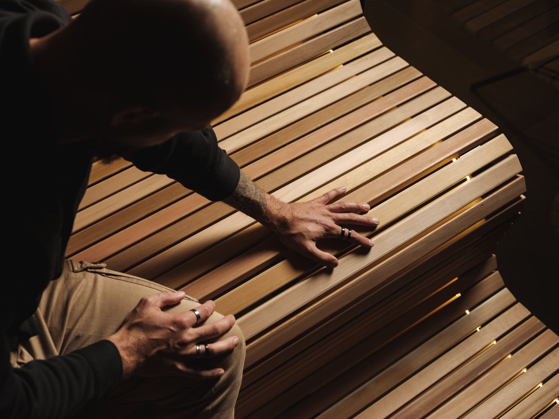 Ein Tischler von Deisl streicht über eine geschwungen Saunabank um die Qualität zu prüfen.