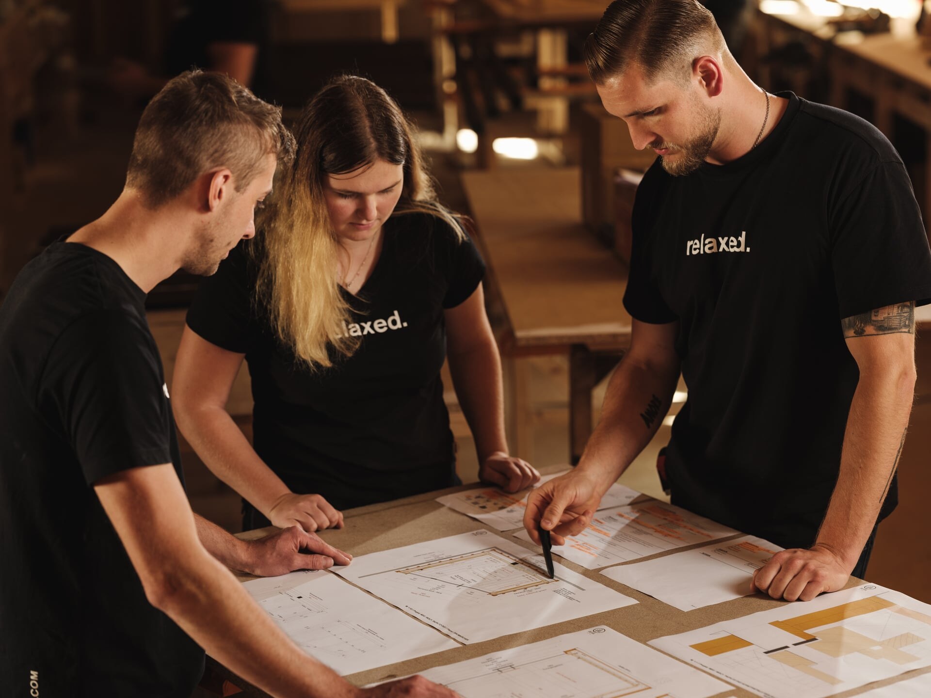 Ein Tischlerteam von Deisl bespricht an einem Werkstatttisch den Produktionsplan einer Sauna.