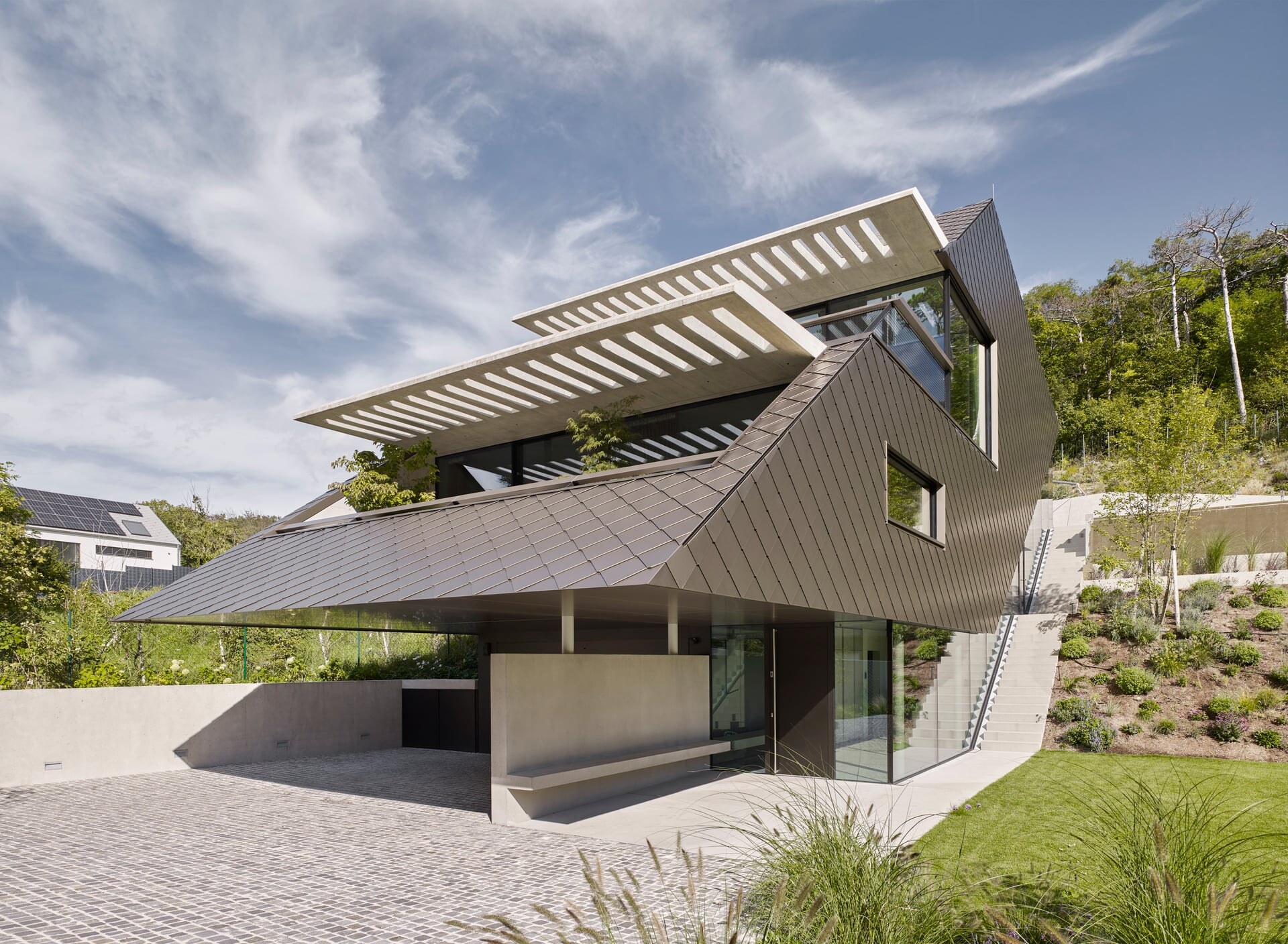 Modernes Architektenhaus mit mehrerern Terrassen und braungold verkleiderter Fassade in neinem Garten.
