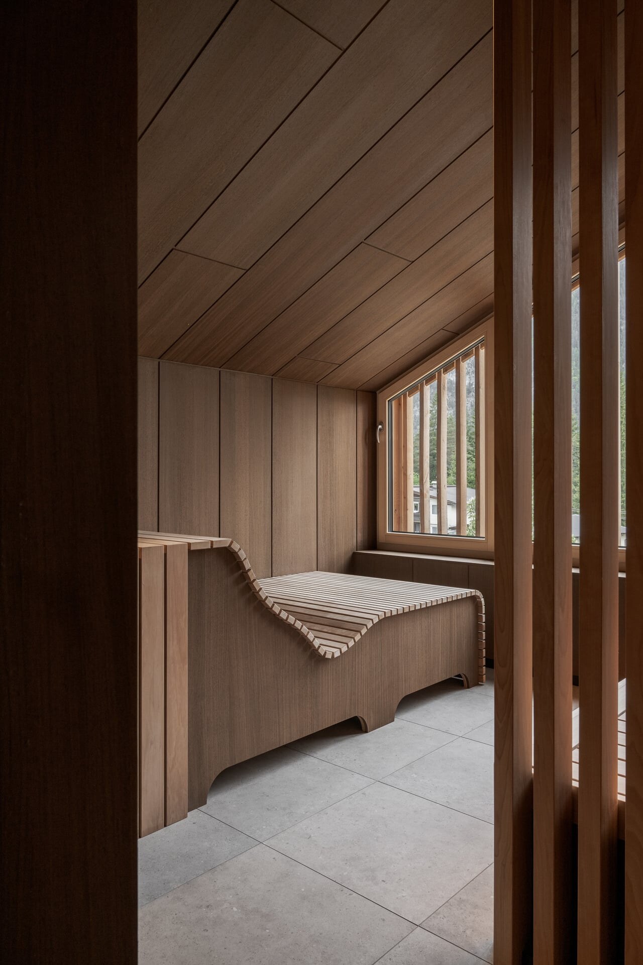 Ergonomisch geschwungene Saunabank in einer Sauna aus dunkler Thermeoesche unter einer Dachschräge.
