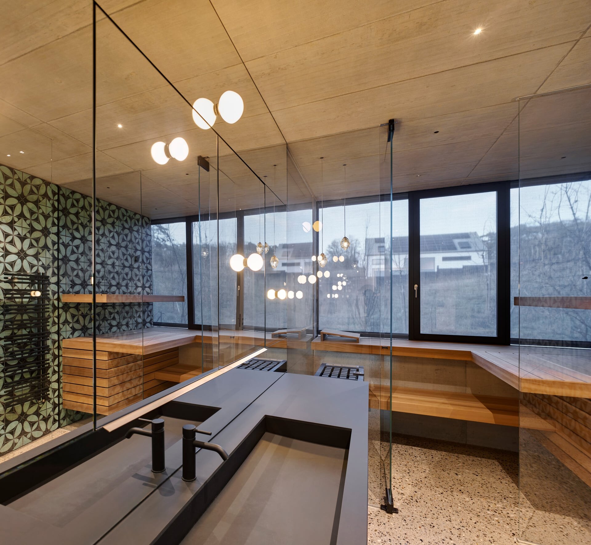 Moderne Luxussauna aus Glas in einem Badezimmer mit schwarzem Waschtisch eingebaut.