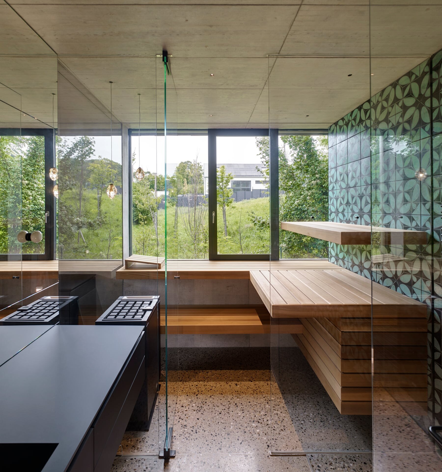 Moderne Sauna aus Glas mit Fliesenwand und Zedernholzbänken in einem Badezimmer mit Blick ins Grüne.