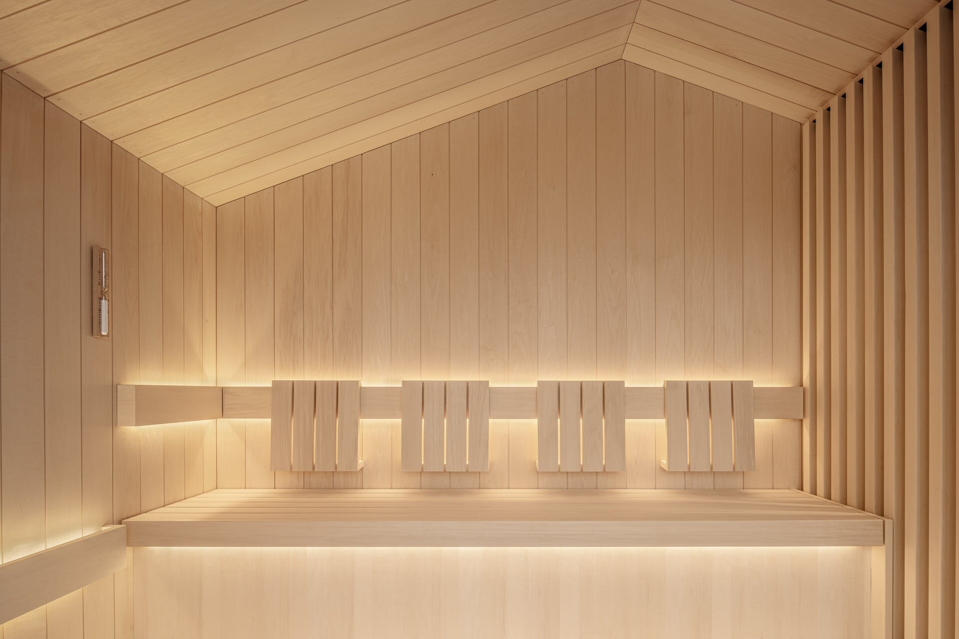 Minimalistische Design-Sauna aus hellem Espenholz unter einem Dachgiebel mit dezenter Beleuchtung.
