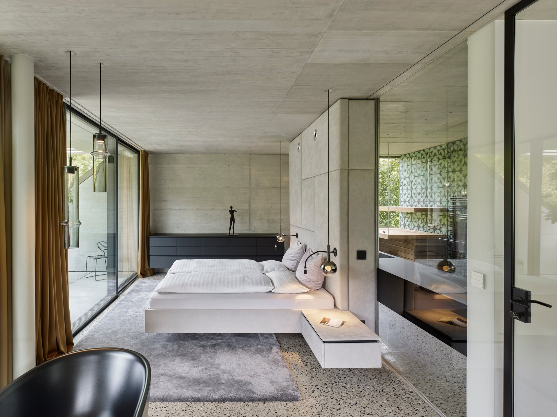 Minimalistisches Schlafzimmer aus Sichtbeton und Terrazzo mit Blick ins Badezimmer mit Sauna.