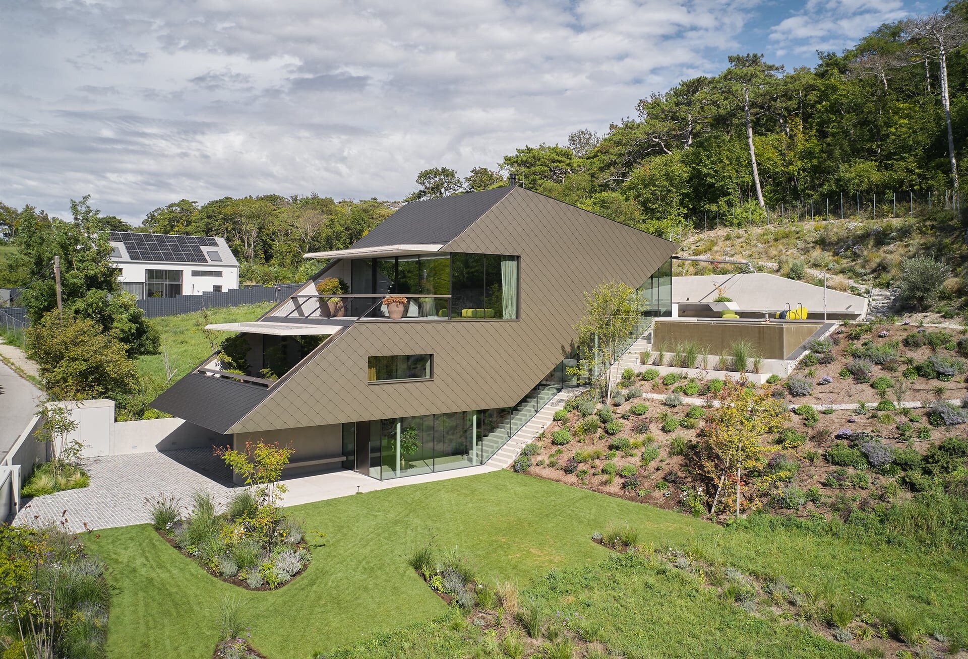 Privates Anwesen mit modernem Haus in Hanglage und verkleideter Fassade.