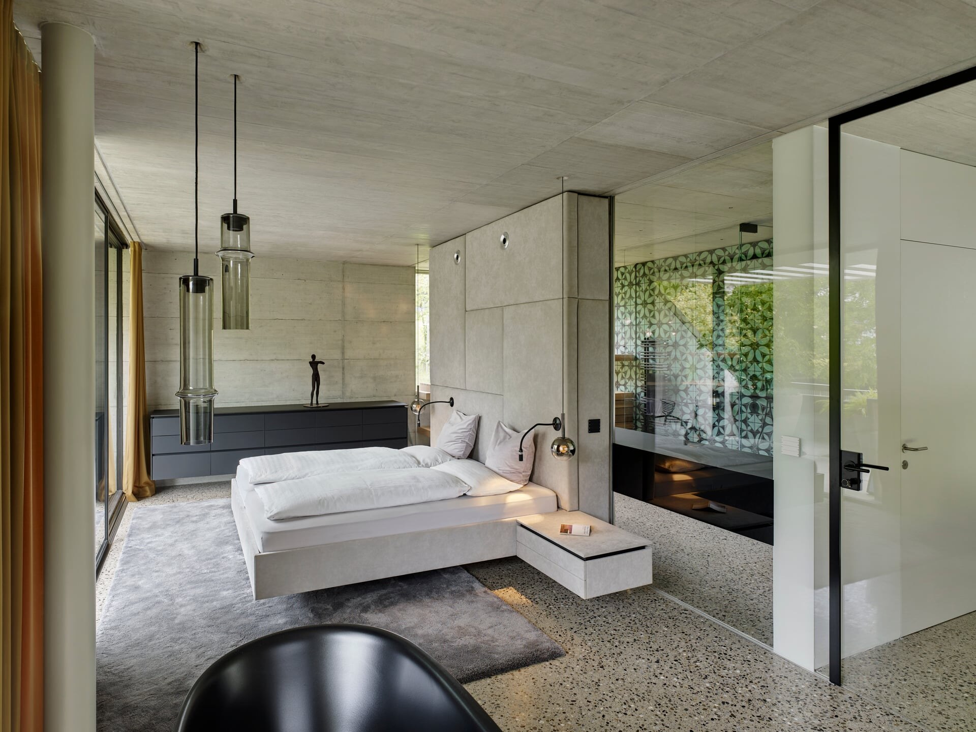 Modernes Schlafzimmer aus Sichtbeton mit Blick ins angrenzende Bad mit Sauna.