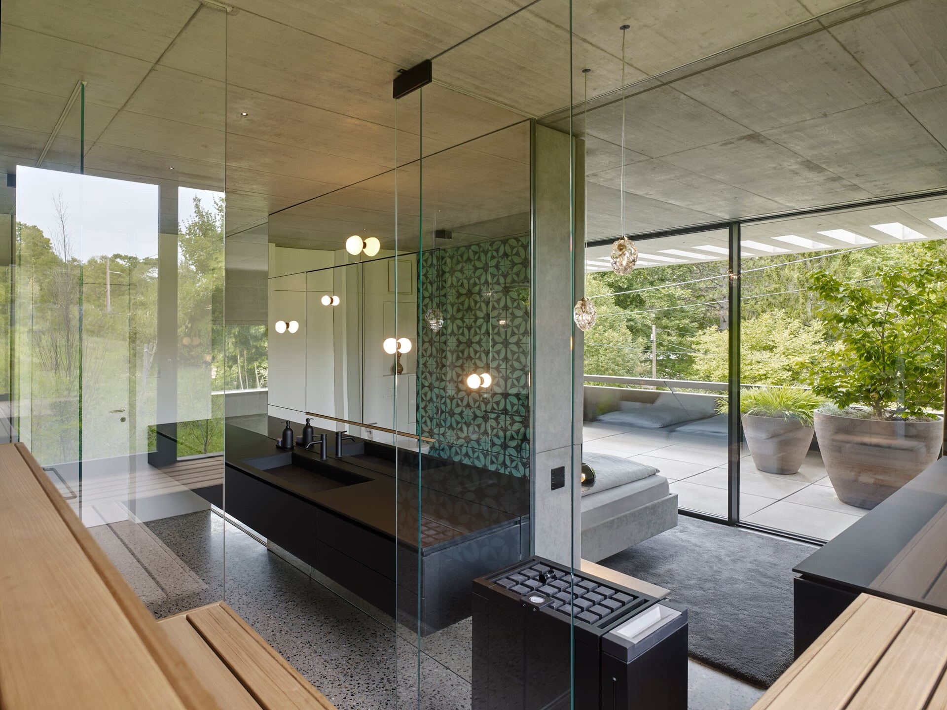 Ausblick aus einer voll verglasten, modernen Sauna in ein offen angelegtes Badezimmer mit Terrassenzugang.