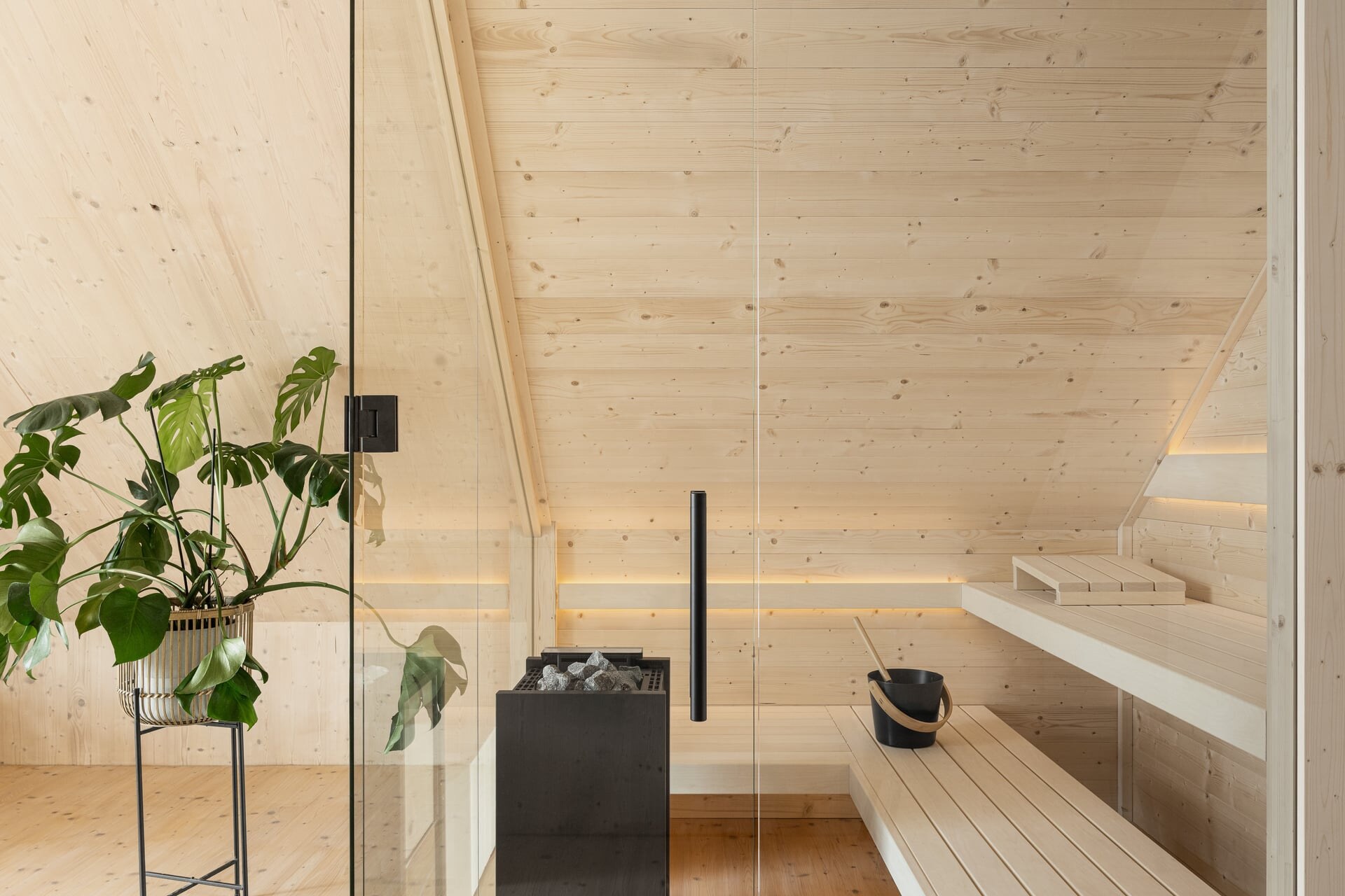 Minimalistische Sauna aus naturbelassenem, hellen Fichtenholz mit großer Glasfront unter einer Dachschräge integriert