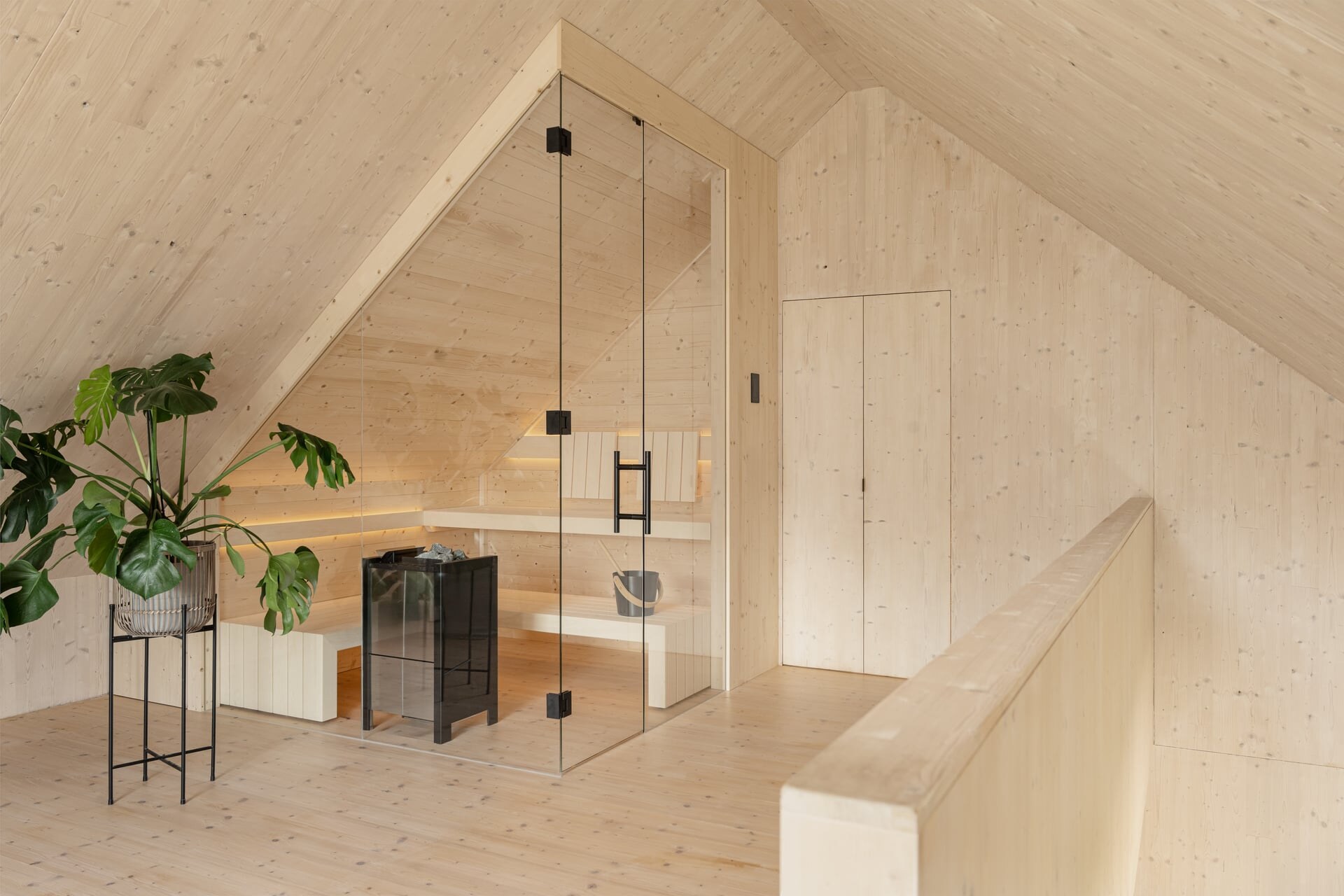 Minimalistische Sauna im Scandi-Stil aus massivem Fichtenholz mit raumhoher Glasfront, harmonisch unter einer Dachschräge eingebaut