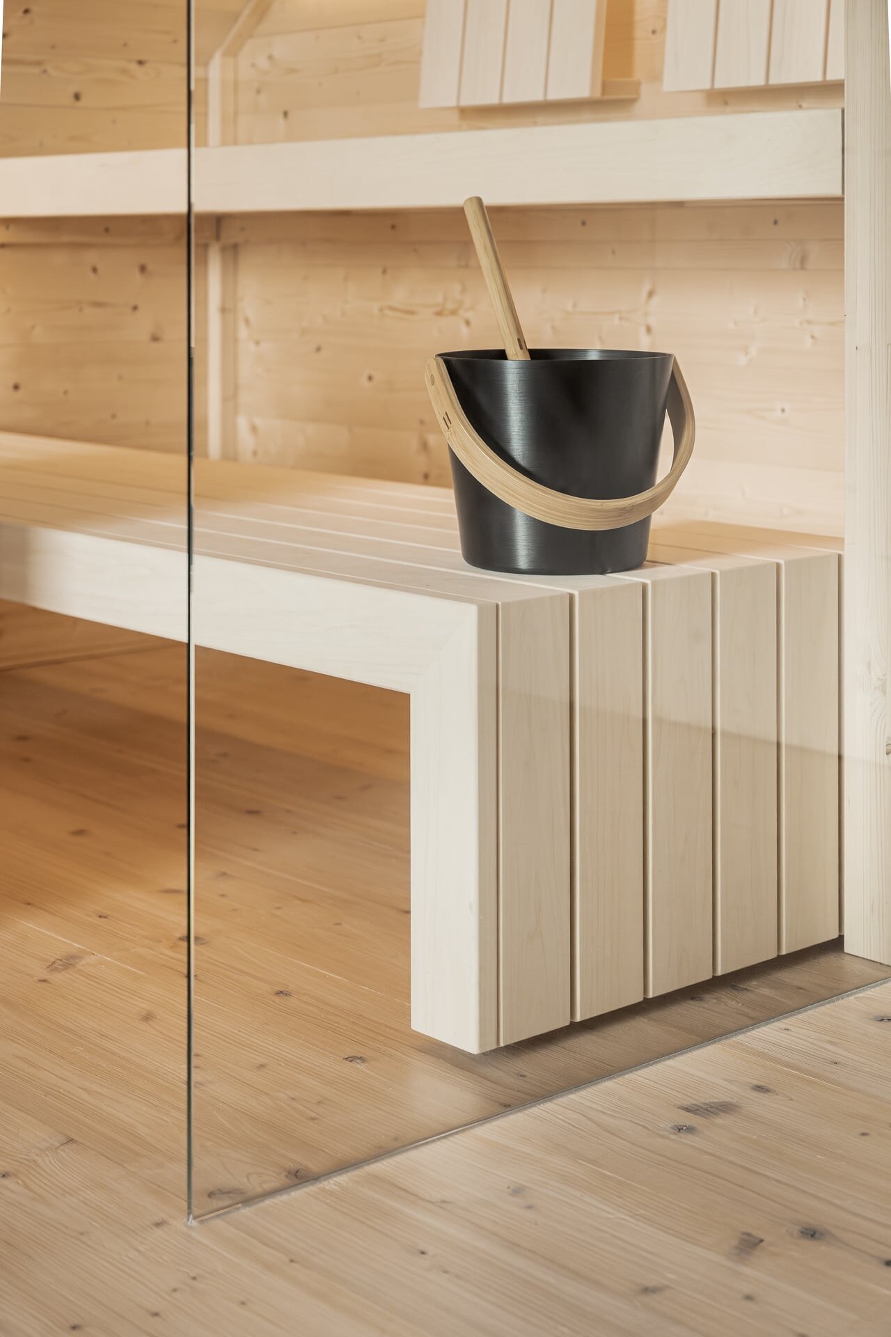 Moderne Saunabank in minimalistischem Design aus hellem Espenholz mit schwarzem Saunakübel