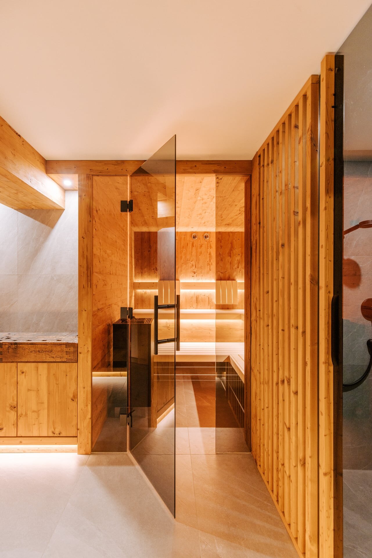 Moderne, verglaste Sauna in rustikalem Holz-Dsign mit getönter Glasfront und indirekter Beleuchtung.