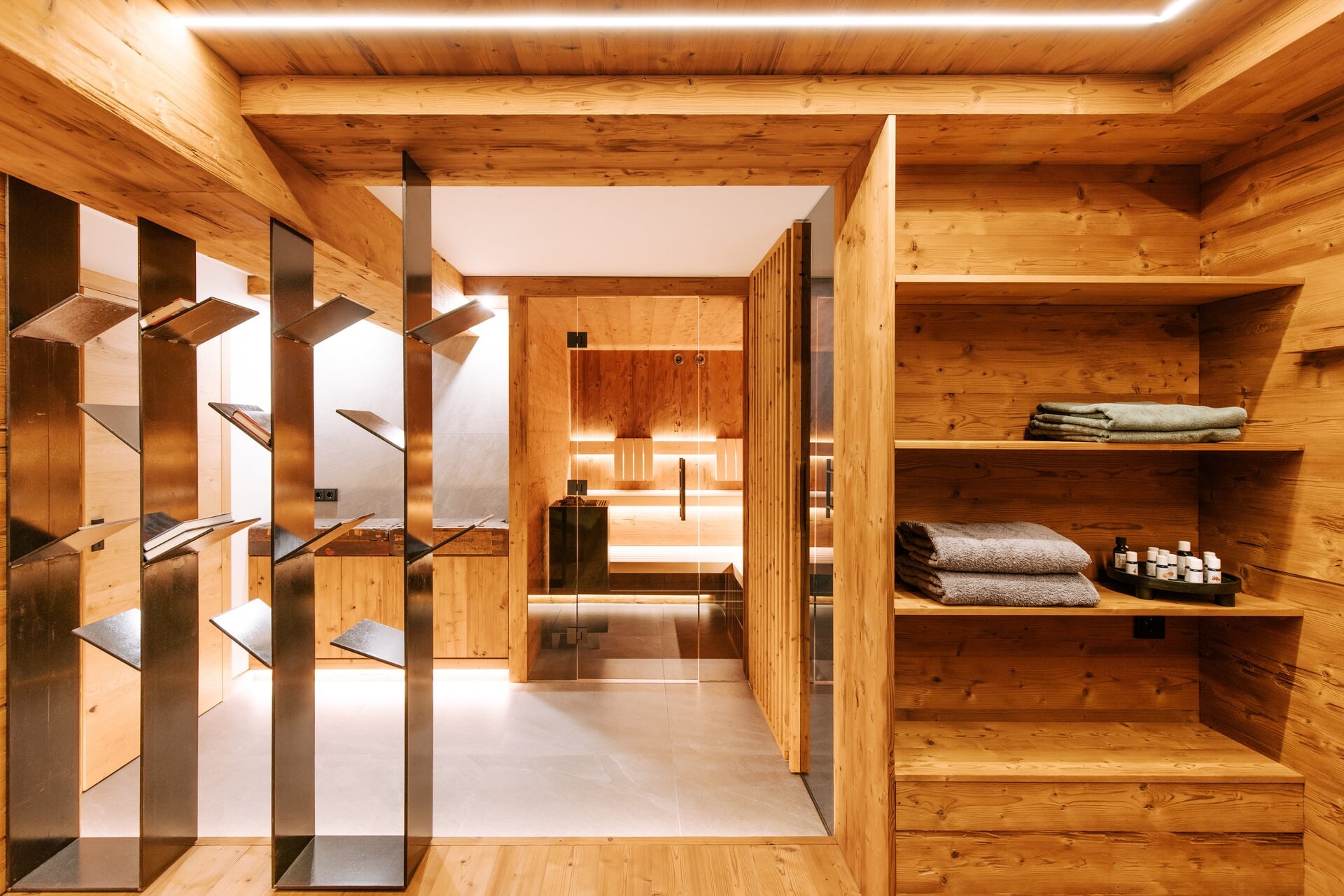 Moderner Wellnessbereich im Keller in rustikal alpinem Stil mit beleuchteter Sauna und Raumteiler aus Metall als Magazinablage.