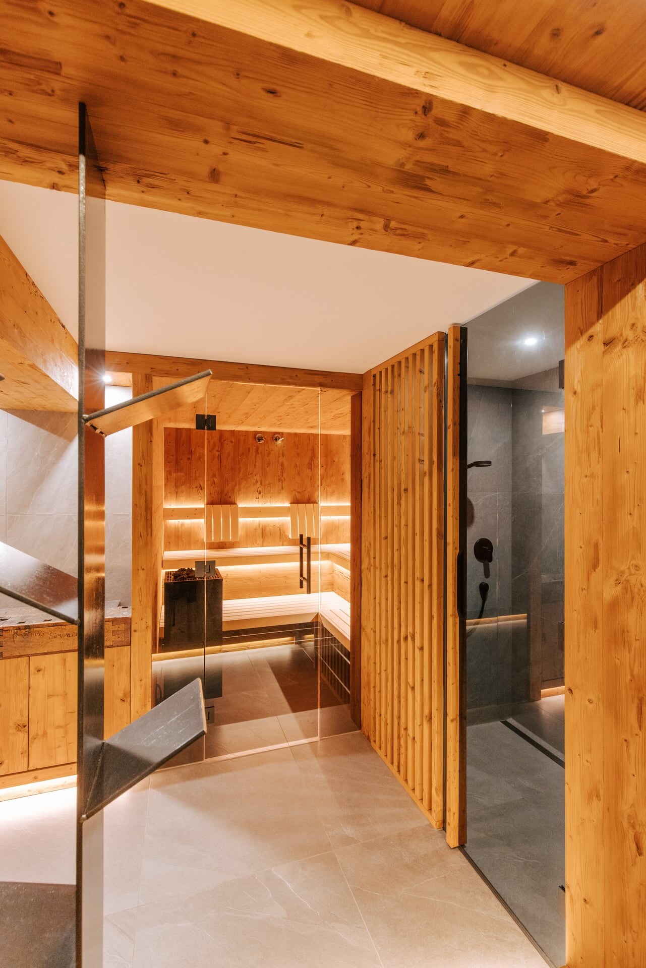 Moderner Wellnesskeller mit Sauna in rustikalem Design aus gehacktem Holz, mit grauen Fliesen und einer Duschnische mit getöntem Glas.